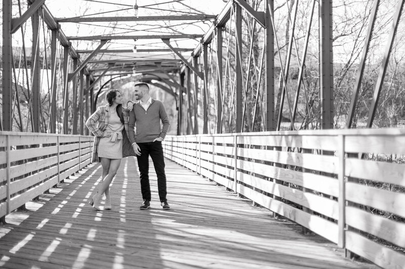 Engaged couple standing together on the Iron Bridge near the Phoenixville Foundry in a timeless black-and-white photo.
