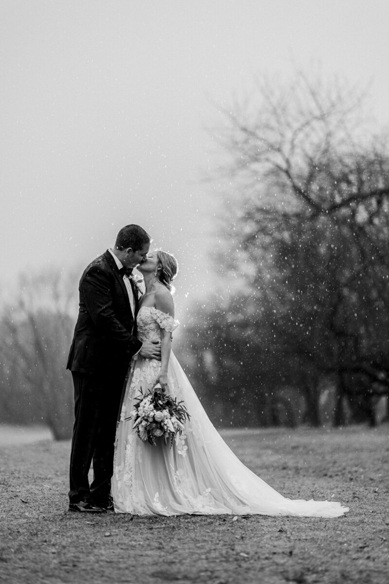 Black and white photo of a bride and groom kissing under bare winter trees at their Hudson Valley elopement