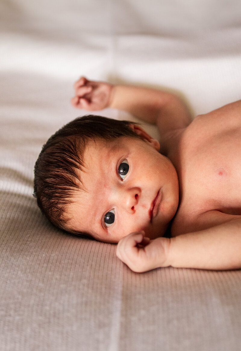Newborn baby lays in the bed and stares at the photographers camera