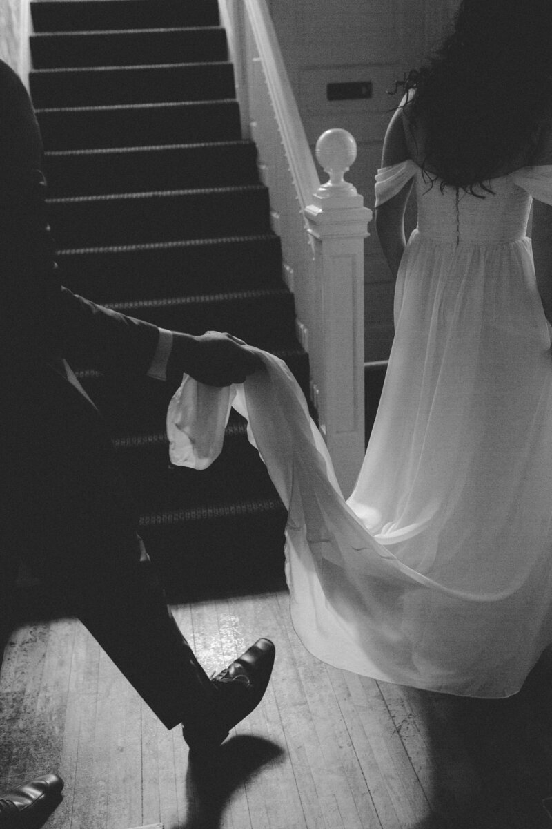 Groom carefully holds the bride's train as she walks through the historic Bell Hill venue, capturing a timeless, romantic moment.