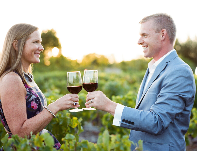 The couple in the vineyards, romantic pose drinking red wine at the sunset
