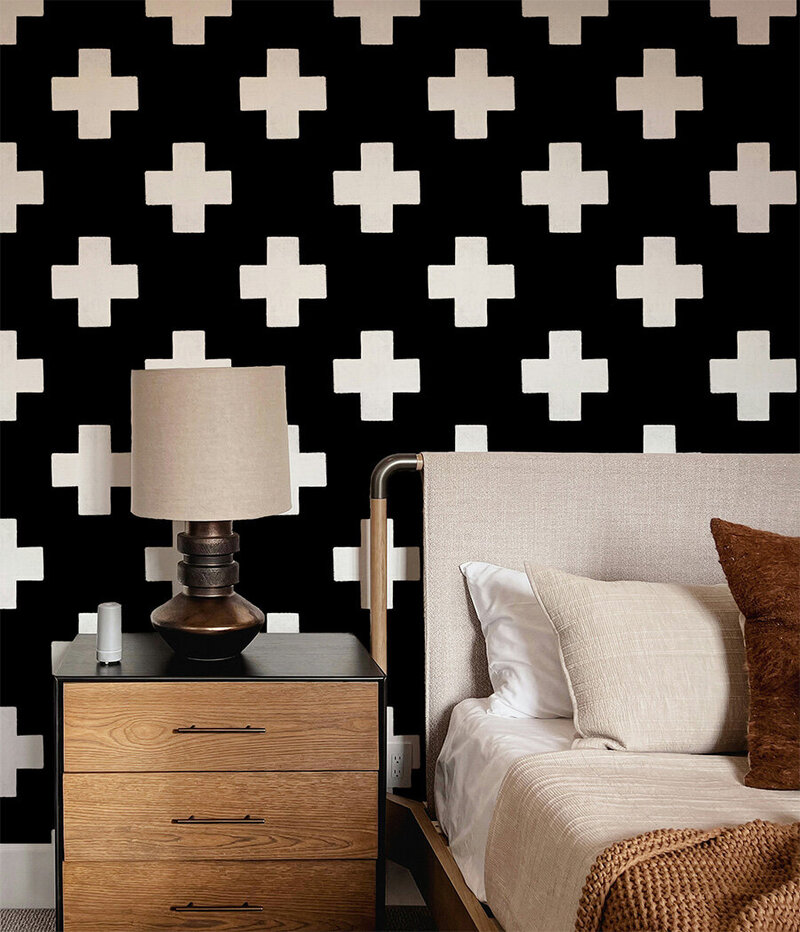Black colored wallpaper with symmetrical tiles in the form of hand drawn white Swiss crosses adorn the walls of a bedroom with masculine furniture. Style bohemian, modern, vintage modern, Scandinavian