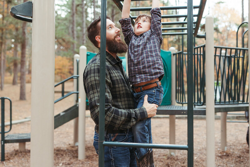 Father helping son cross the monkey bars at the park in Farmington, Missouri during a lifestyle family portrait session with Jennifer Mosier Photography. 