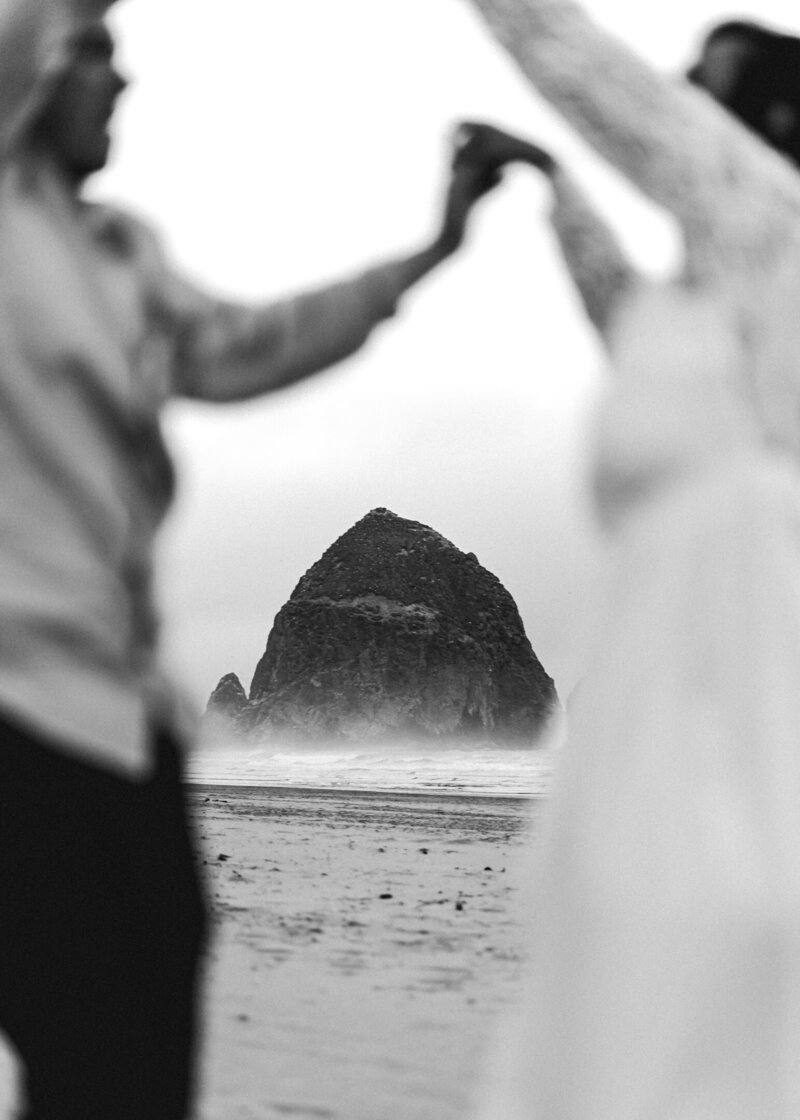 During their Oregon coast elopement, a couple frames the iconic haystack rock as they dance in celebration