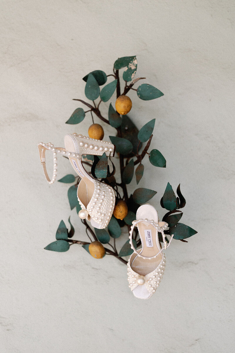 Elegant bridal shoes displayed on a citrus tree at Dallas Arboretum. A fine art wedding detail with a European-inspired aesthetic