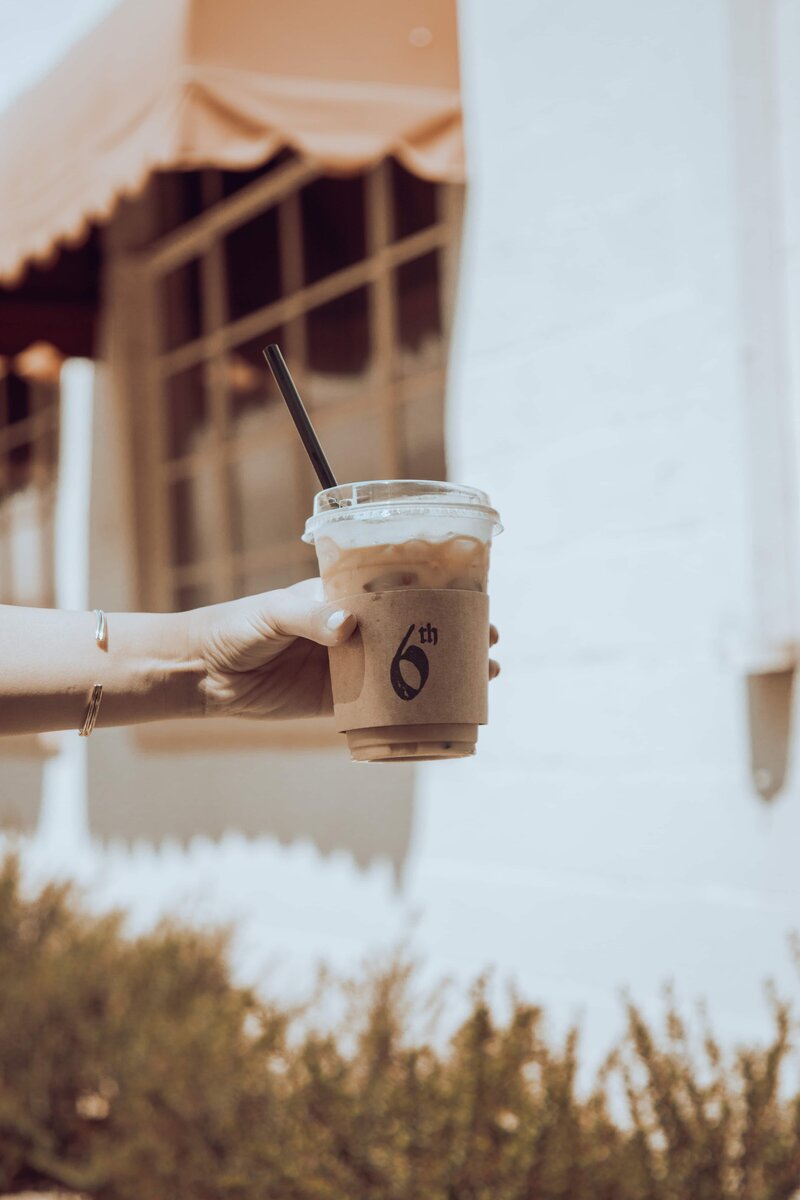 Hand holding out ice coffee with 6th logo