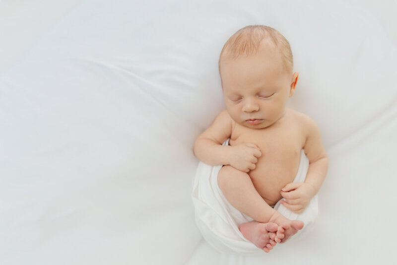 Newborn baby is swaddled and sleeping with his hand touching his face during his newborn session