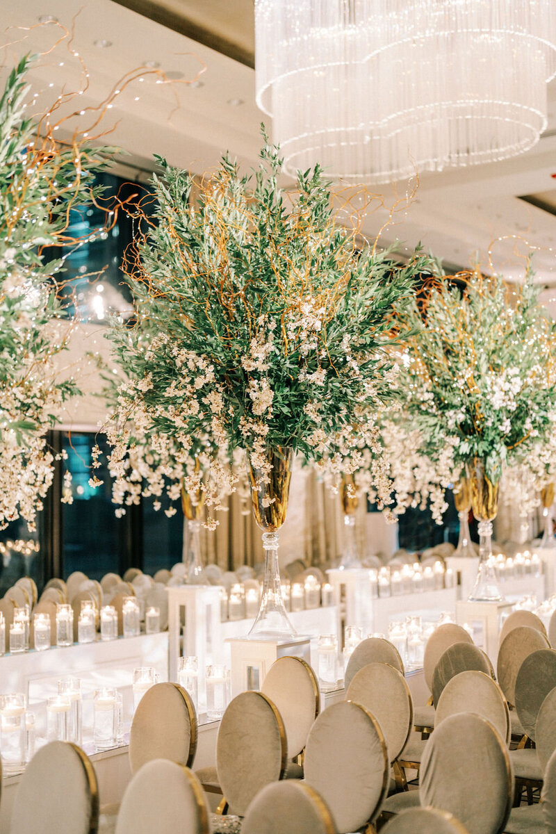 An opulent wedding reception at The Langham Chicago, featuring tables adorned with tall floral centerpieces and candles under a grand, tree-inspired decor with twinkling lights.