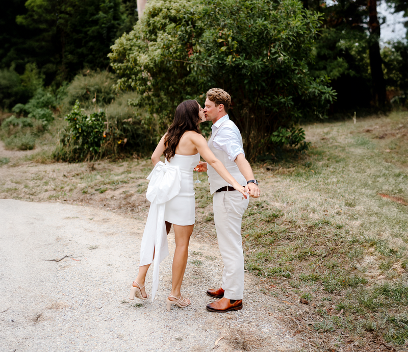 Bride and Groom get a sneaky kiss as they wander along a gravel road