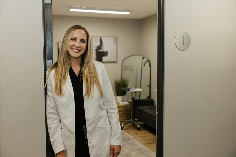 The founder of RMWC, Kylee Johnson, is leaning against the doorway of one of the rooms at the clinic. She's wearing a white lab coat and smiling casually.