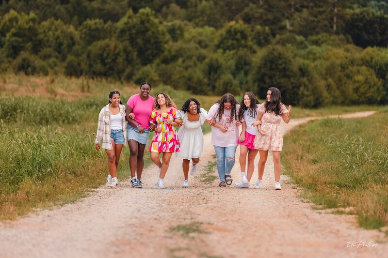 Group of teen girls walking down a dirt road linking arms. 