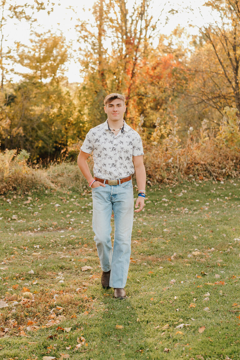 Graduating senior boy walking through a field during sunset.