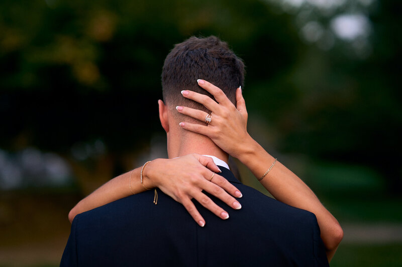 a wedding ring on the finger of a bride who is holding her grooms head