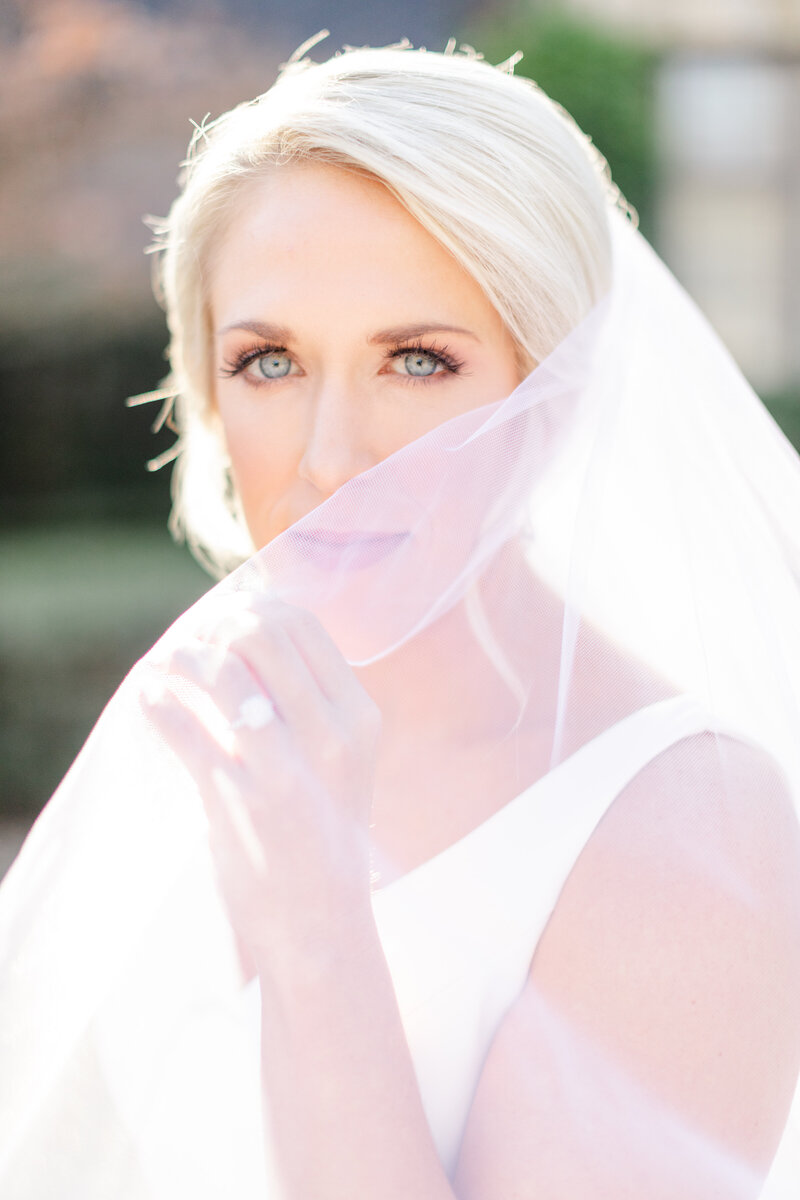 bride with blonde hair and blue eyes looking into camera with veil covering half of her face