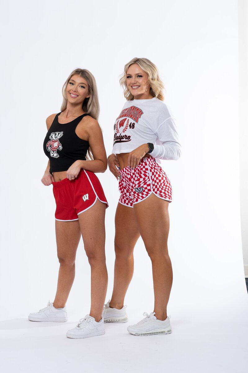 two models wearing solid red and checkered shorts with college logo in corner