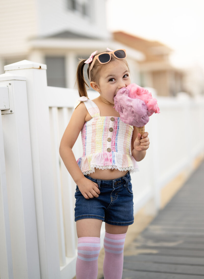 Outdoor birthday photoshoot of girl eating cotton candy on boardwalk. Birthday Photo session was captured by Jenni Nikki Photography.