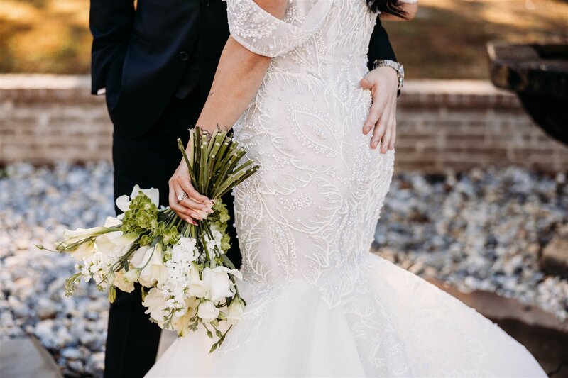 Details of the bride's dress, flowers, and shoes as she stands by the large  glass window of the glass chapel in Northwest Arkansas