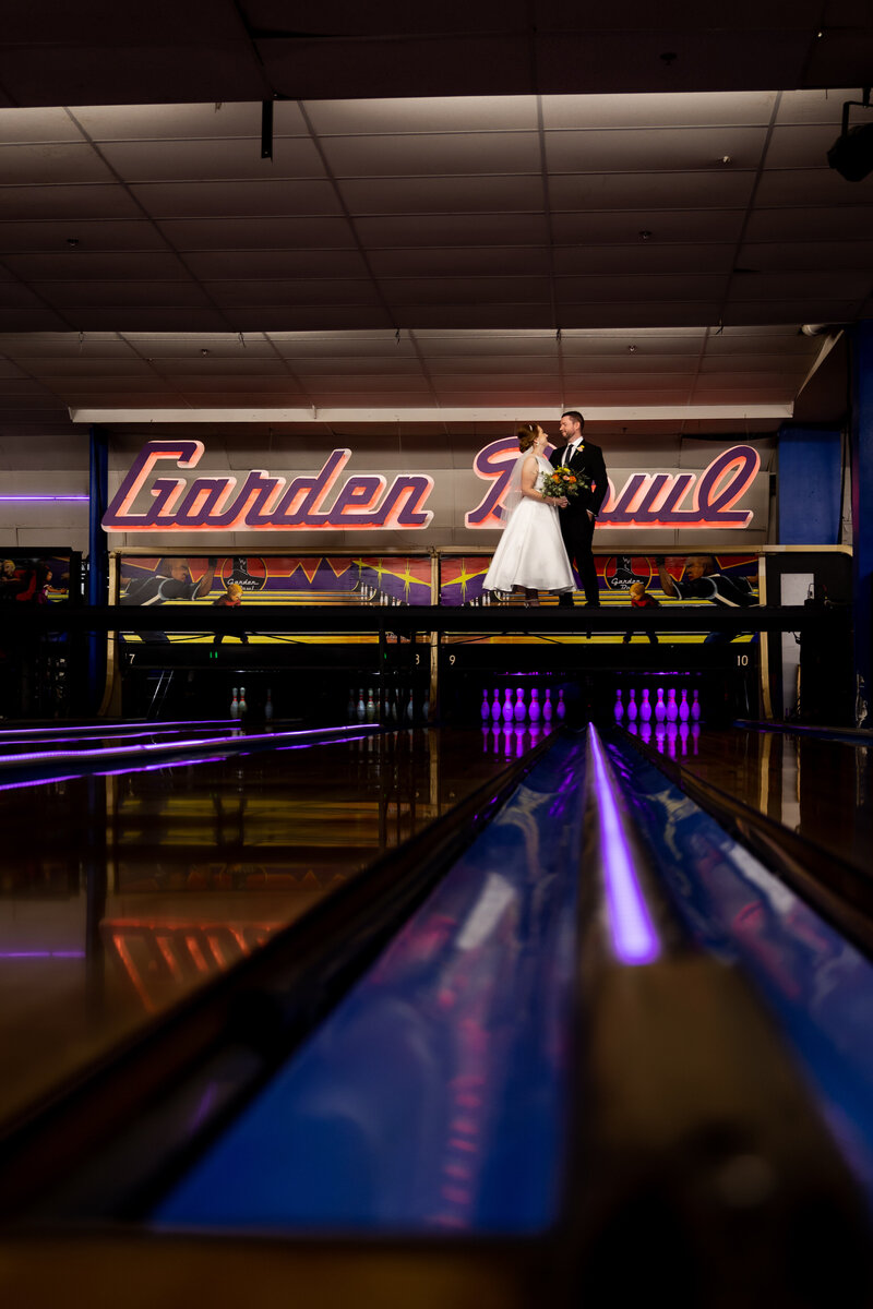 Couple on bowling alley lane in their wedding attire.