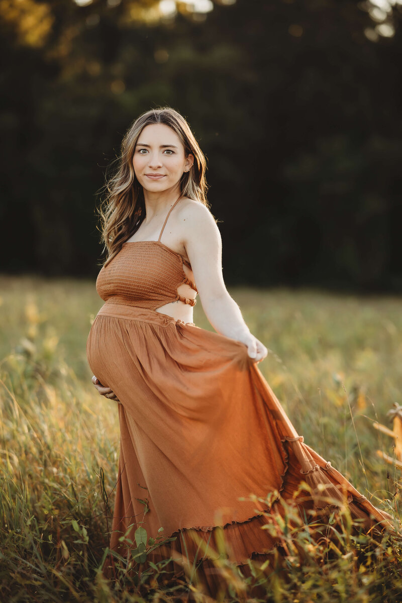 A radiant expecting mother in a delicate lace dress cradles her belly while standing in a tranquil field at sunset, captured by a Harrisburg maternity photographer.