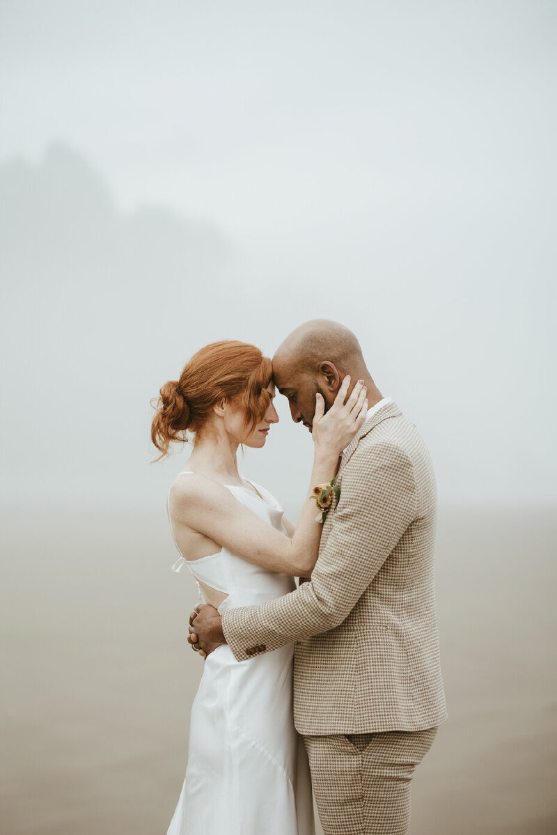 bride and groom on beach looking into each others eyes
