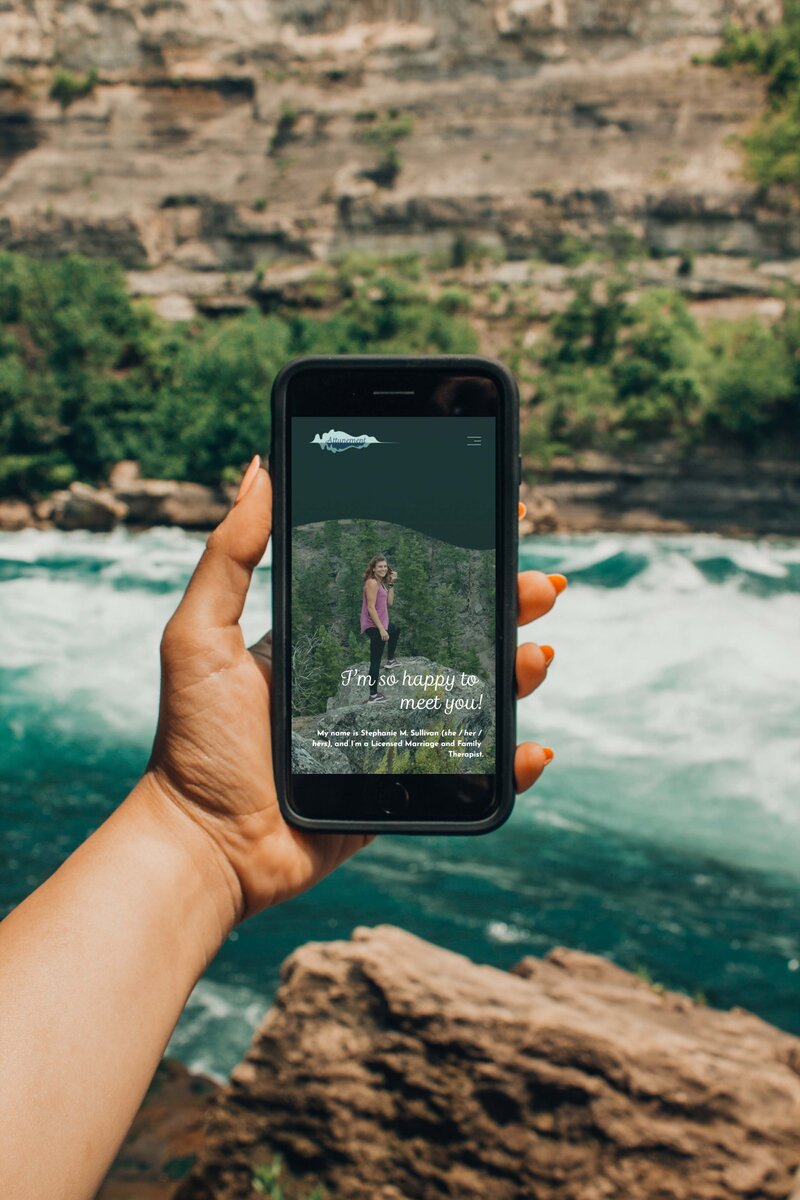 This image shows the top of the Attunement "About Me" website page on a smartphone, showing Stephanie Sullivan standing on a cliff edge. The text beneath her reads "I'm so happy to meet you!"