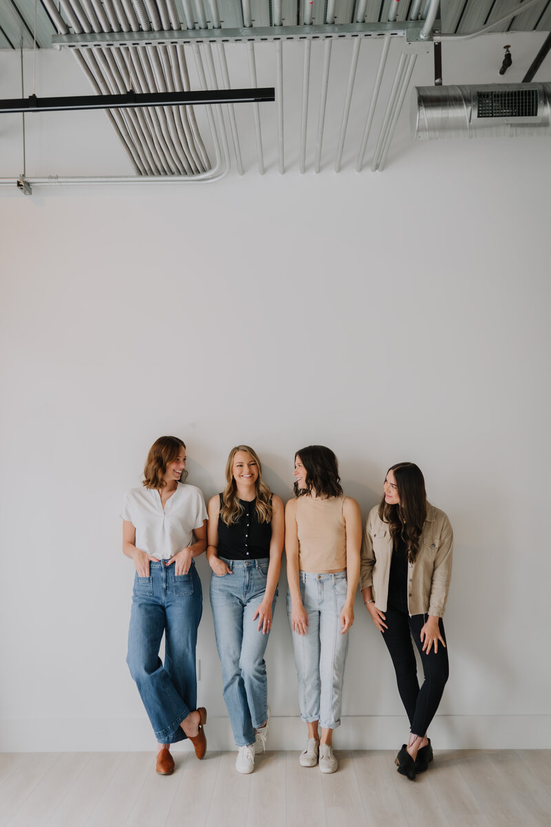 Four women standing against a wall