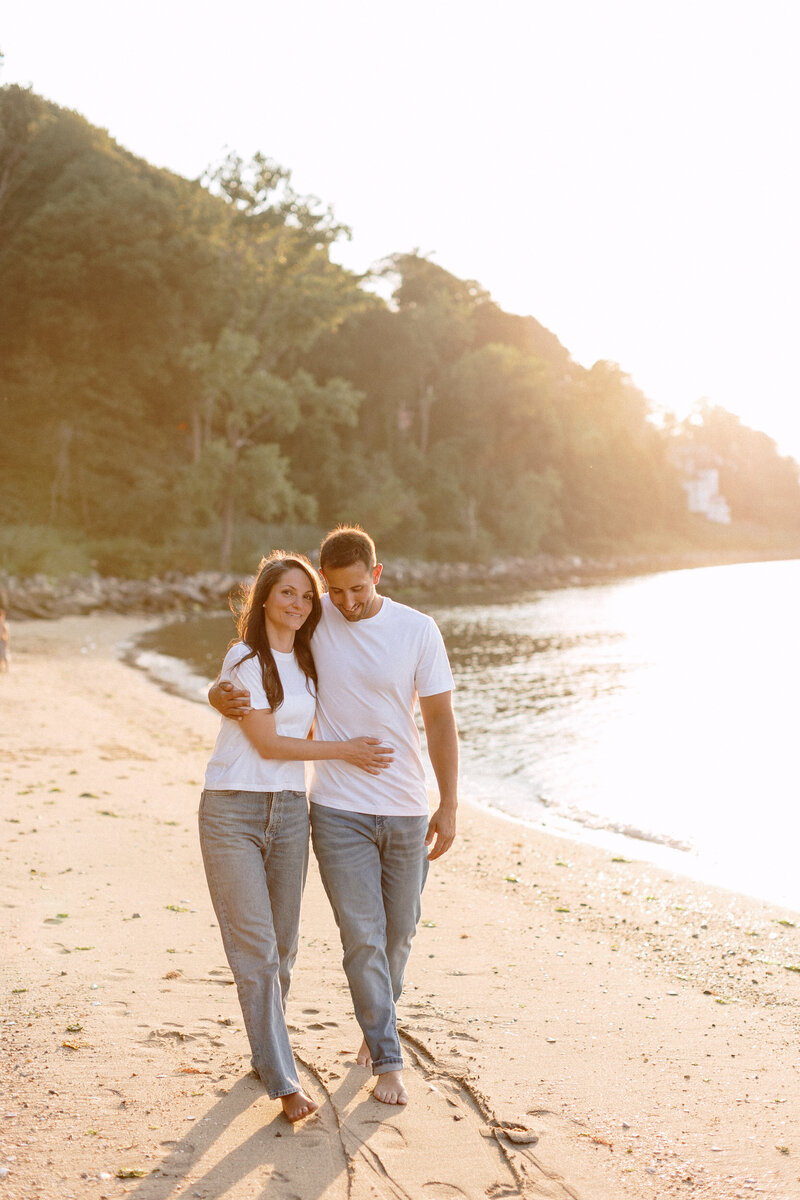 Engagement photos of a couple at the beach, smiling and enjoying the moment with the ocean waves gently lapping nearby.