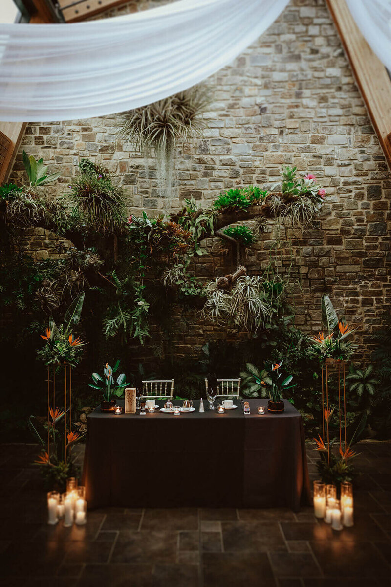 Sweetheart table decorated with flowers, candles, and gold chairs.