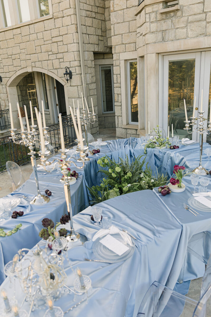 Editorial tablescape with blue linens and tall candelabras set against stone architecture at Greystone Castle in Boulder, Colorado.