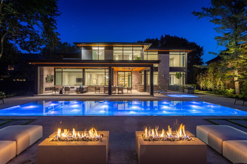 luxury big window home in hamilton ontario with a lit backyard pool at nighttime and a firepit