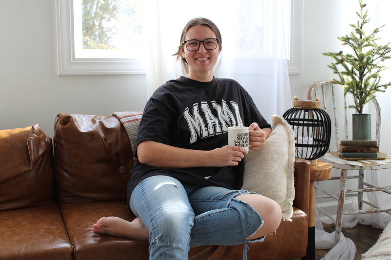 Mckayla S, owner of the Comma Mama Co. white woman with brown hair wearing a black "mama" tee and jeans.