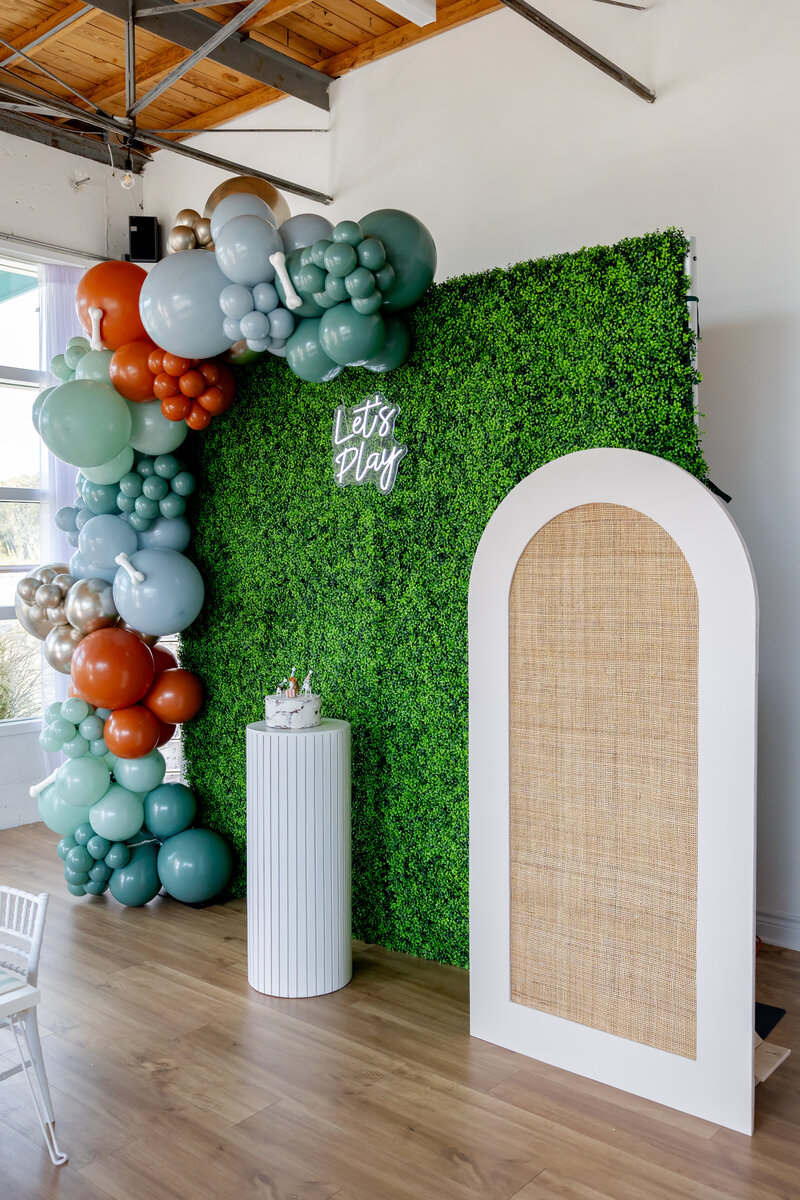 Dog party decorated wall with neon sign, rattan arch, cake stand and balloon garland.
