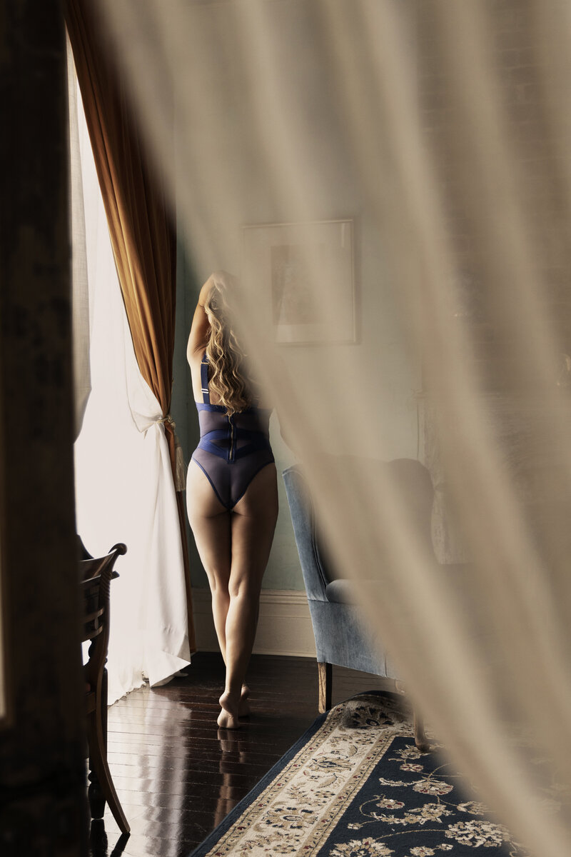 Woman in a red robe leaning on an old window frame in a New Orleans studio