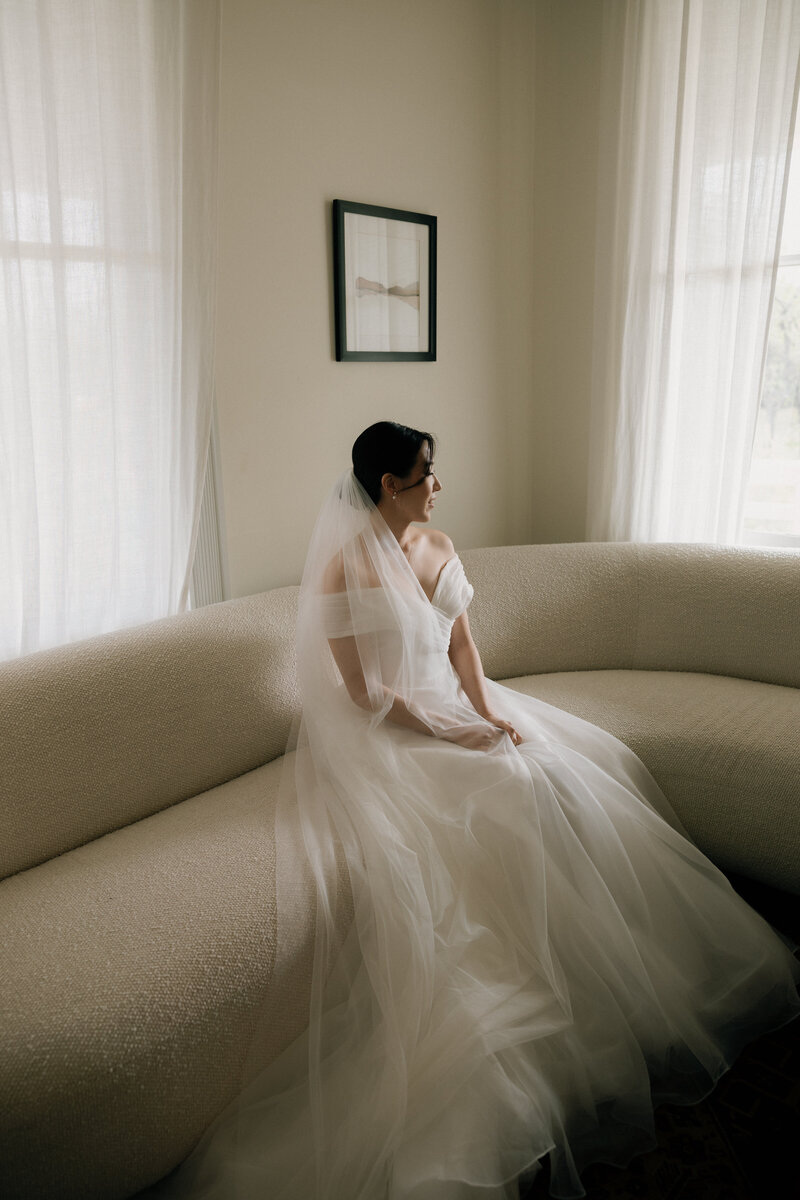 Portrait of bride sitting on a couch with windows on either side