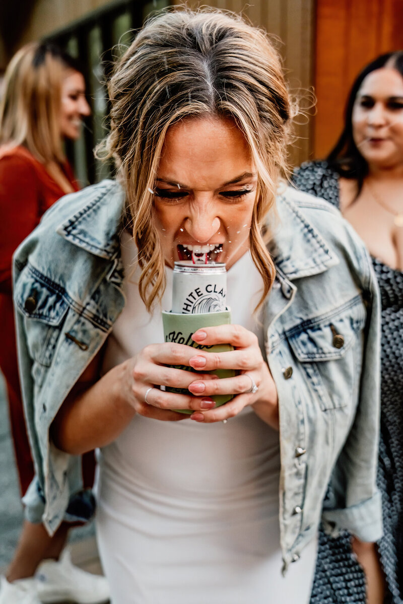 Bride cracking open a White Claw at her wedding reception, candid moment by Washington wedding photographer Aim True Photography