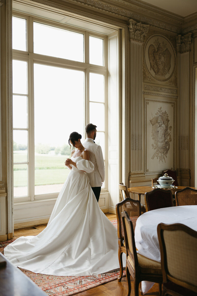 Bride and groom standing back to back for their first touch in the french chateau Domaine du Réveillon in the countryside of Burgundy France, by Andrea-Marie Photography