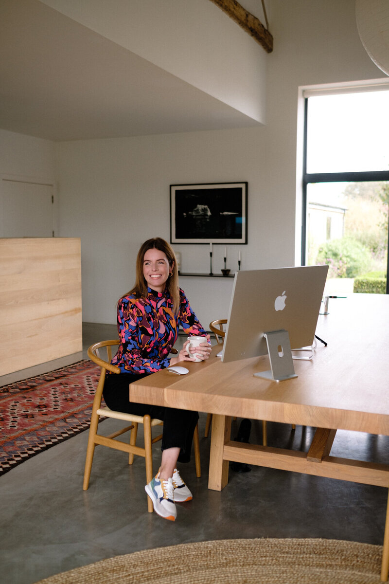 A woman sitting at a desk, focused on her work with a laptop and coffee in front of her.
