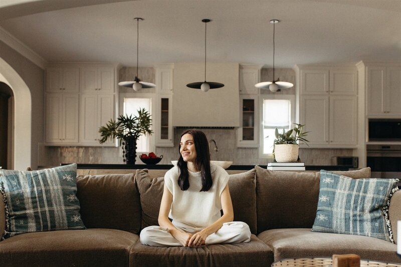Hope Danyla sitting on a brown couch in a modern home, designed by Hope Miriam Designs in DFW