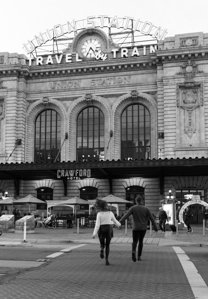 Black and white documentary style photo of couple running through downtown denver for their Union Station engagement session