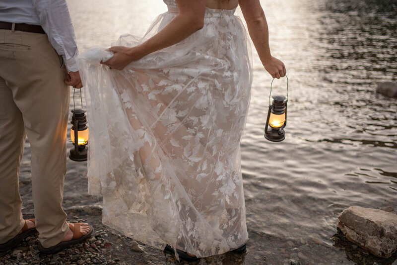 Couple's hands holding lanterns while they wade into lake