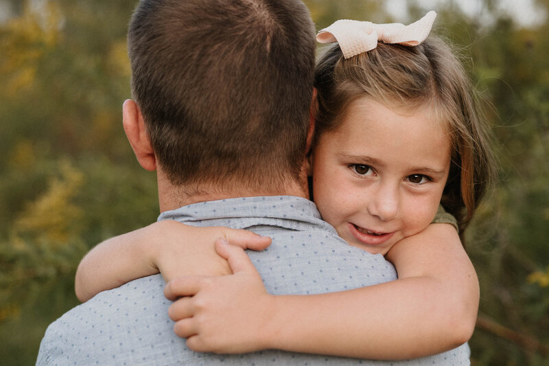 daughter wrapping arms around dad's neck and peeking over shoulder