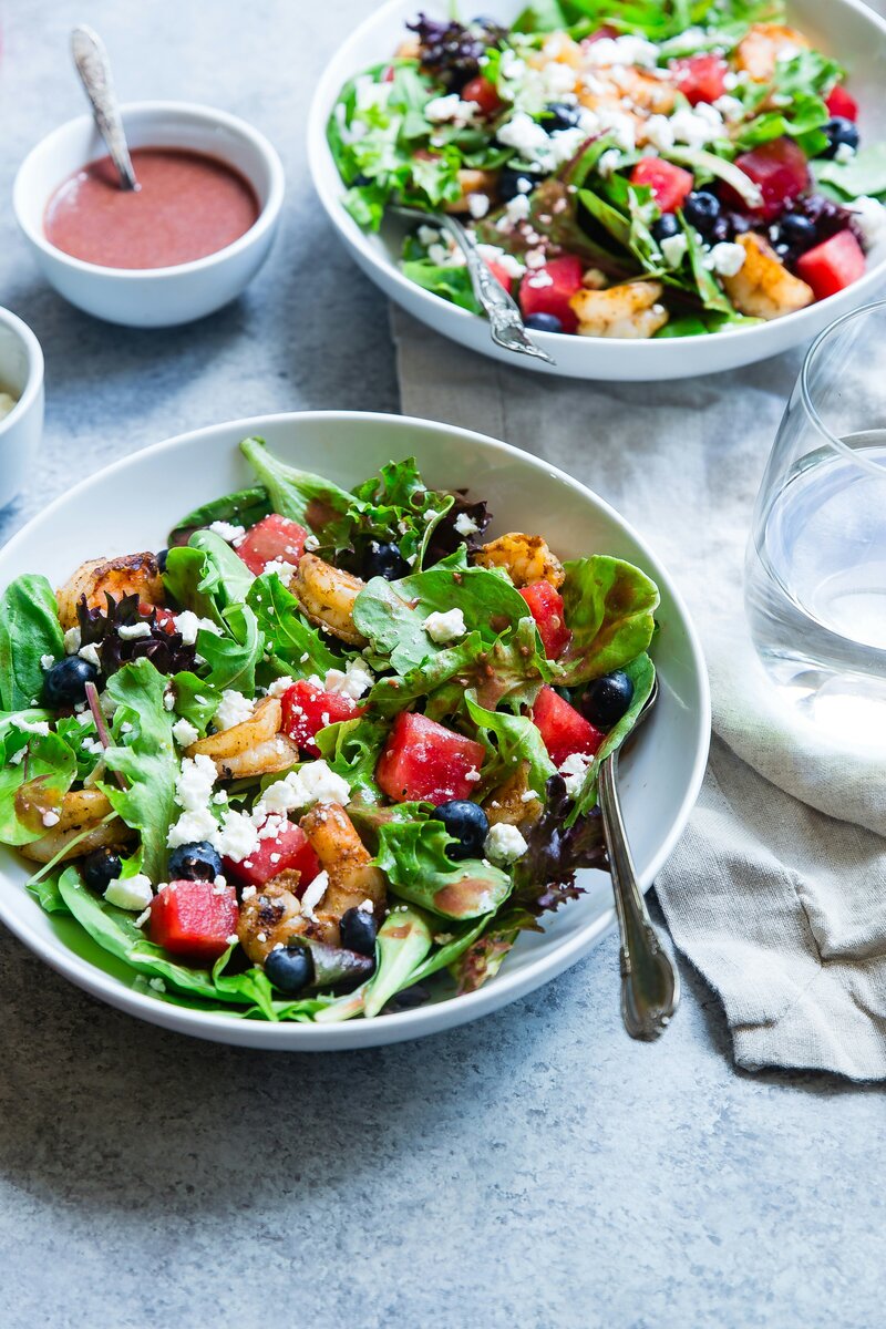 Bright, colorful salads in bowls next to small bowls of dressing