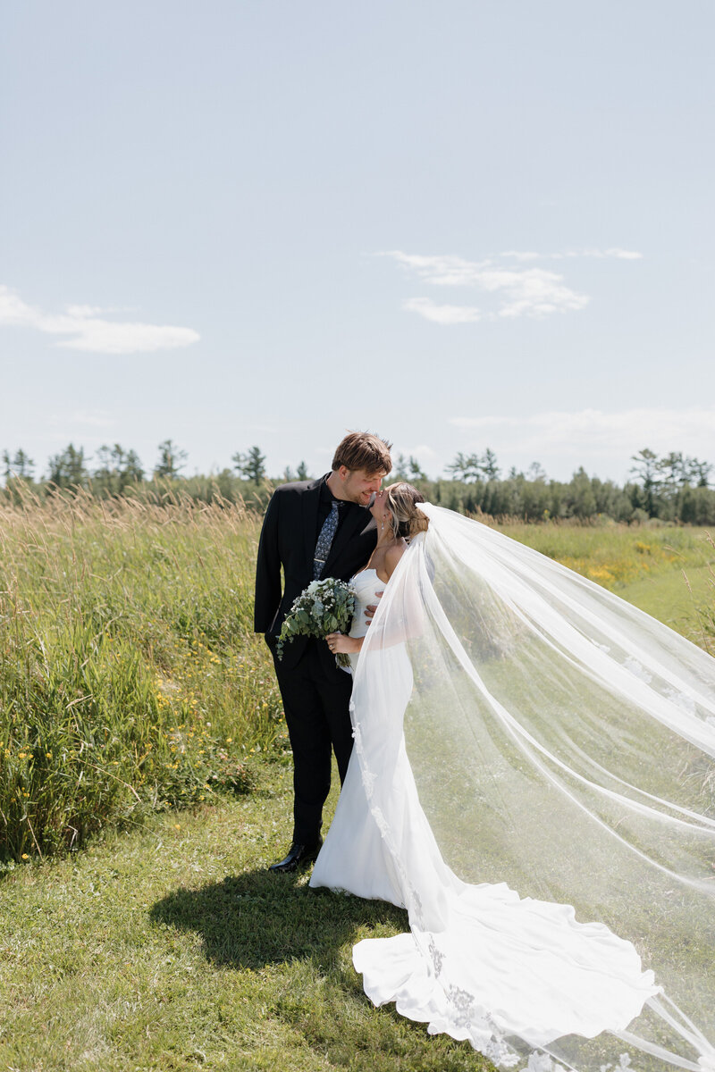 A newlywed couple kissing as they stand in a field 
