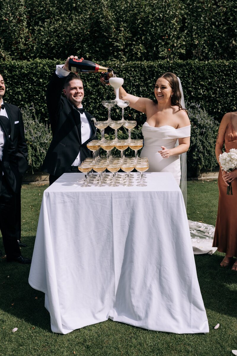 a bride and groom pour a champagne tower at their queenstown wedding