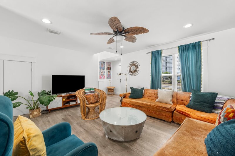 Relaxed TV area in vacation rental featuring rattan chairs, teal and mustard seating, and fun wall art with a coastal vibe.
