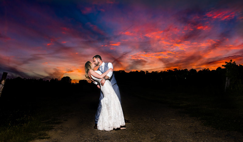 Bride and groom kiss under a colorful sunset