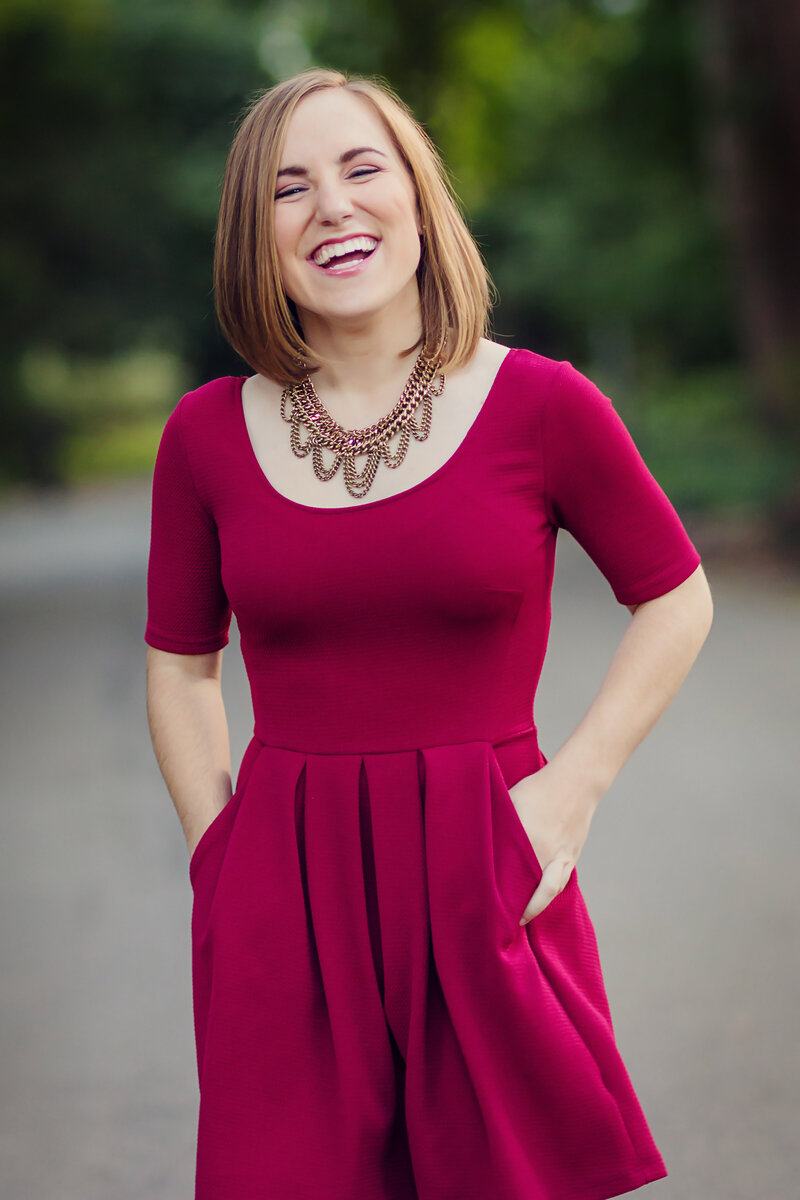 Senior portrait of a girl laughing in a bright pink dress and ornate gold necklace.