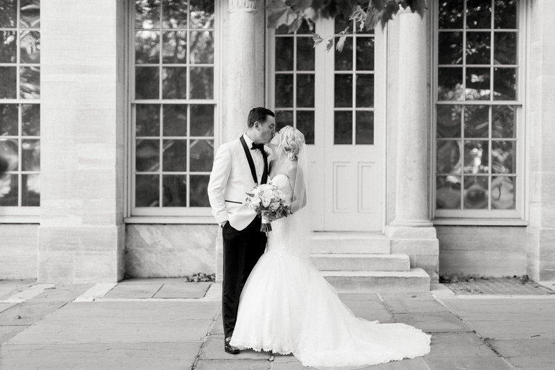 black and white image of bride and groom kissing in front of the merchant exchange building in philadelphia