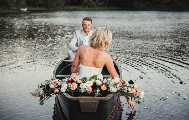 a bride and groom in a canoe together with the bride reaching one hand into the water
