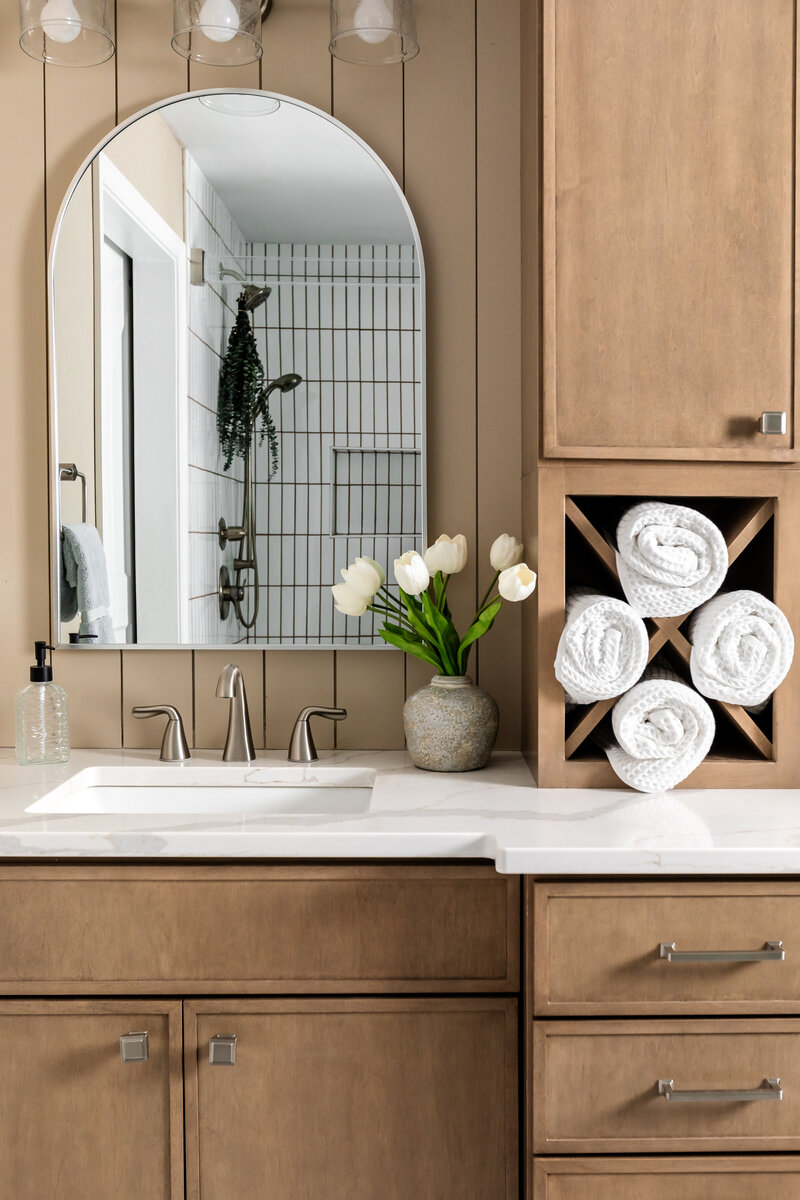 Primary bathroom stained neutral brown vanity cabinet with tower storage, mirror and decor.